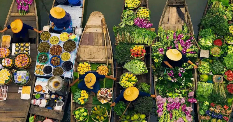 Barcos de madeira repletos de frutas tropicais coloridas navegando pelos canais estreitos de um Mercado Flutuante tailandês