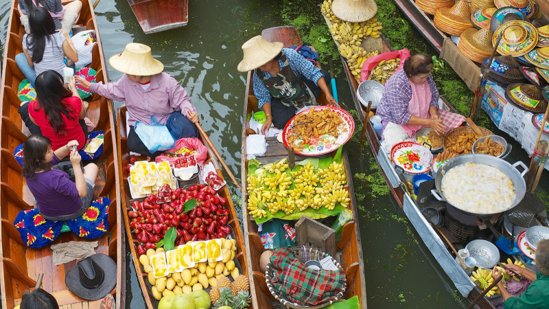 Barcos de madeira repletos de frutas tropicais coloridas navegando pelos canais estreitos de um Mercado Flutuante tailandês
