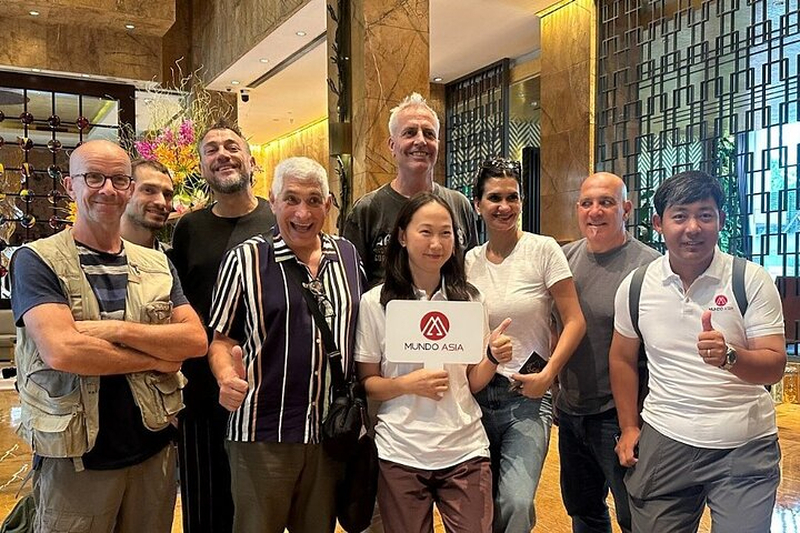 Guia de turismo da Mundo Asia Tours segurando uma bandeirinha e sorrindo enquanto orienta um grupo de visitantes no aeroporto