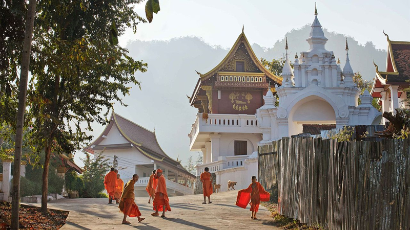 Monges em vestes laranjas caminham silenciosamente pelas ruas de Luang Prabang ao amanhecer