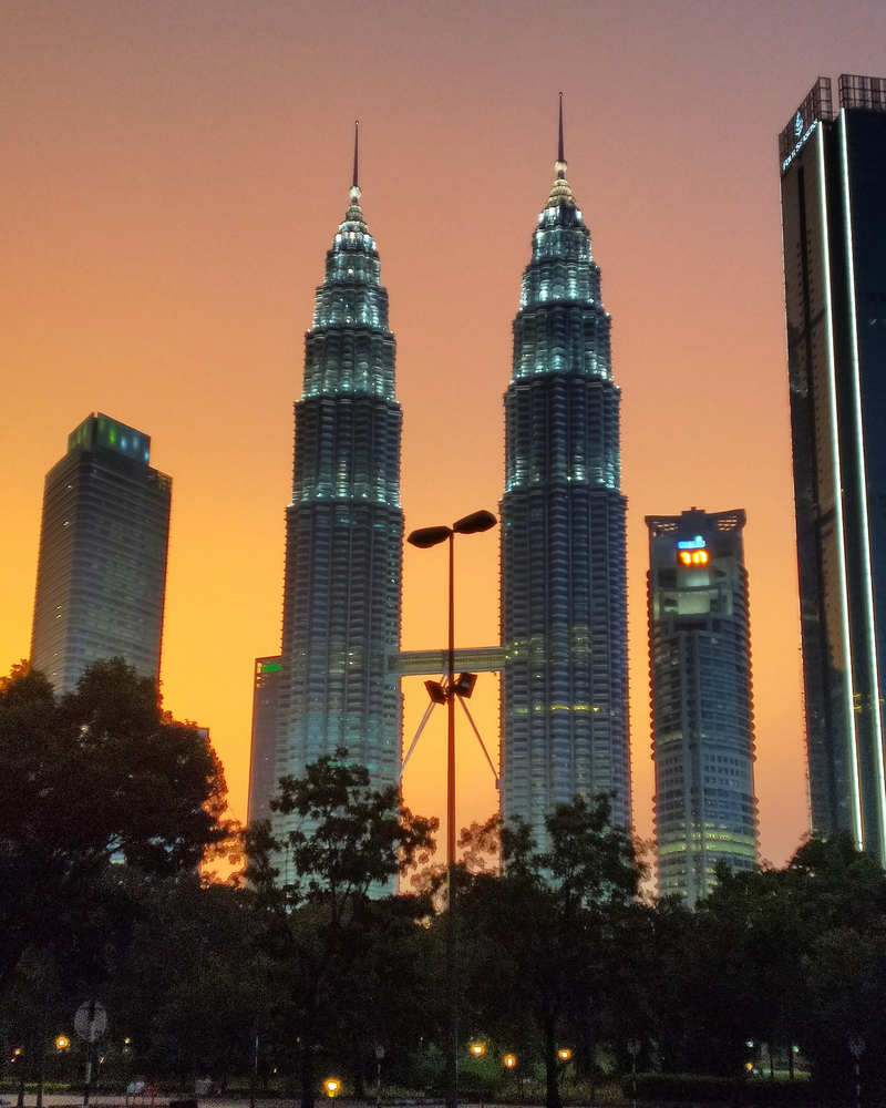 O sol reflete nas imponentes Torres Petronas em Kuala Lumpur durante um entardecer de céu claro